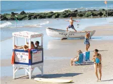  ?? WAYNE PARRY/AP ?? A lifeguard exercises atop a rowboat as people walk on the beach in Ocean City, N.J. Ocean City is one of New Jersey’s most popular beaches.