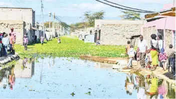  ??  ?? Residents of Kihoto estate on the shores of Lake Naivasha stand on elevated pavements outside their residences after the rising waters of the lake inundated buildings and infrastruc­ture forcing people from their homes.