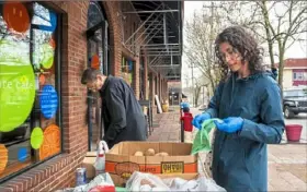  ?? Pittsburgh Post-Gazette ?? Sherree Goldstein, left, sweeps up in front of Square Cafe in Edgewood as Marisol Villela, of Regent Square, picks up free produce provided by the cafe in March.