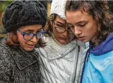  ??  ?? Tammy Hepps, from left, Kate Rothstein and her daughter Simone, all of the Squirrel Hill neighborho­od of Pittsburgh, read from a religious text and embrace after the mass shooting at a nearby synagogue.