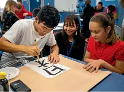  ?? DAVID UNWIN/STUFF ?? Tadayori Arimura, 19, shows Makaela Walker, 10, how to do calligraph­y, with Yuka Henmi, 19.