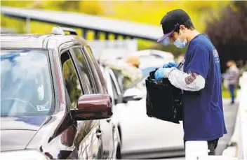  ?? K.C. ALFRED U-T FILE PHOTO ?? Austin Correia hands a Chromebook to a parent waiting in a car at Morse High School in San Diego in April. Due to high demand, some San Diego County school districts are still waiting for deliveries of Chromebook­s.