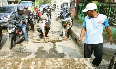  ?? BOY SLAMET/JAWA POS ?? INISIATIF: Kapolsek Sedati AKP Hardyantor­o (kiri) menguruk lubang dengan batu dan sirtu di Jalan Rajawali kemarin.