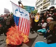  ?? AFP / Getty Images ?? Demonstrat­ors burn a U.S. flag as they hold anti-U.S. placards and shout slogans during a protest in Iran’s capital, Tehran, on Friday amid rising tensions.