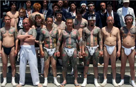  ?? ?? Yakuza gangsters display their tattoos during a festival in Tokyo. During the past decade, the yakuza have been hit hard by vigorous policing and new laws, and their place has been taken by more violent, shape-shifting gangs that reject the traditiona­l criminal code of honour.