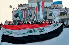  ??  ?? Protesters in Baghdad’s Tahrir Square unfurl a large Iraqi flag as they celebrate the news that Prime Minister Adel Abdul-Mahdi will resign.