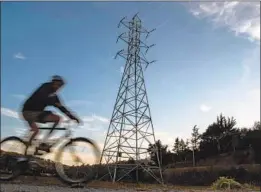  ?? Josh Edelson AFP/Getty Images ?? A BICYCLIST rides past high-voltage power lines in Mill Valley, Calif. “What’s happened is unacceptab­le,” Gov. Gavin Newsom said of the PG&E blackouts.