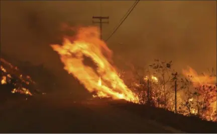  ?? REED SAXON — THE ASSOCIATED PRESS ?? Wind-driven flames from a wildfire race up a slope and cross the road in Malibu, Calif., Friday, Nov. 9, 2018. Known as the Woolsey Fire, it has consumed tens of thousands of acres and destroyed multiple homes