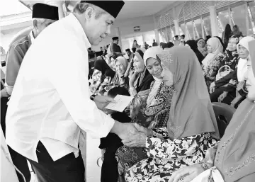  ??  ?? Awang Tengah handing out ‘duit raya’ to one of the single mothers.