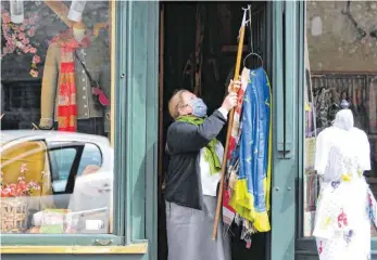  ?? FOTO: BARBARA GINDL/AFP ?? Mit Schutzmask­e, aber wieder im Geschäft: Eine Ladeninhab­erin öffnet erstmals nach dem Shutdown am Dienstag ihre Boutique in der Salzburger Innenstadt.