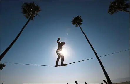  ?? — AFP ?? Beating the heat: A man balancing on a slack rope at Venice Beach, where people have flocked to escape the heatwave in California.