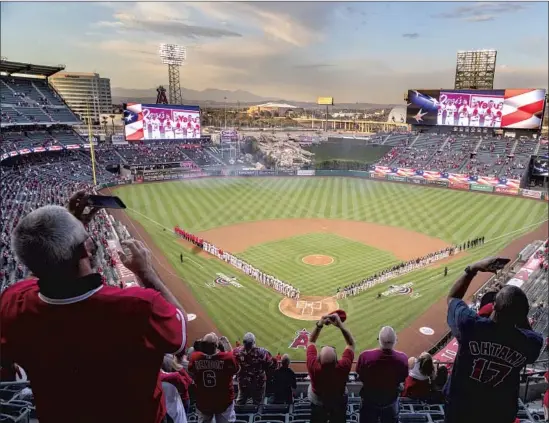  ?? Gina Ferazzi Los Angeles Times ?? ANGELS FANS stand for the national anthem before the season opener Thursday, which featured a spread-out crowd of 13,207 in wide-open spaces at Angel Stadium.