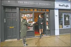  ?? (AP/Alberto Pezzali) ?? Tom, shop manager of Broadway Bookshop, hands off a book order to a customer June 18 outside the shop in Broadway Market, Hackney, in east London. The business started a website in June and converted to collect and delivery to cope with the lockdown measures due to the coronaviru­s outbreak.