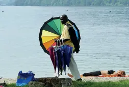  ??  ?? Caldonazzo Ombrelli colorati sotto il sole cocente dell’estate sul lago di Caldonazzo. Il venditore ambulante sfila a fianco di una bagnante per offrire un riparo. Uno scatto che ha impegnato Solomon per ore.