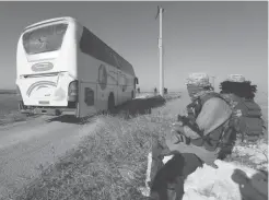  ??  ?? Des membres du groupe jihadiste Hayat Tahrir Al-Cham regardant passer un bus en direction de Foua et Kefraya, deux villages de la province d’Idleb, d’où seront évacuées des milliers de personnes, hier, en Syrie.