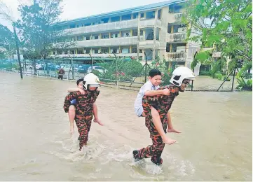  ??  ?? Firemen seen piggy-backing pupils of SJK(C) Tukau near Bakam Road in Miri to the safety of the main road, after rising floodwater forced the school to temporaril­y close yesterday.