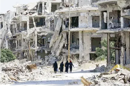  ??  ?? Syrian women walk between destroyed buildings in the regime-held Jouret Al-Shiah neighborho­od of Homs. (AFP)