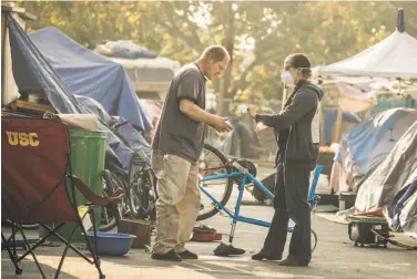  ?? Photos by Paul Kuroda / Special to The Chronicle ?? Whitney Moses hands smoke masks to ex-Marine Tim Green at a homeless encampment in Oakland.