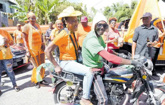  ?? PHOTOS IAN ALLEN ?? A JLP supporter gives a ride to a PNP supporter on his bike in Kellits, Clarendon Northern, on nomination day.