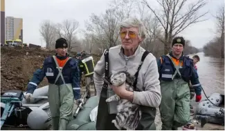  ?? ?? A man holds his cat as he pulls a boat with emergency workers in a flooded area in Orenburg, Russia, Wednesday, April 10, 2024.