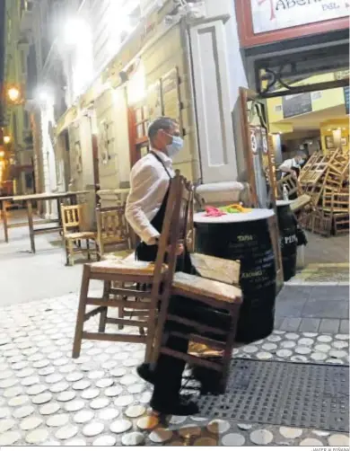  ?? JAVIER ALBIÑANA ?? Un camarero recoge las sillas y las mesas en un bar de Málaga.