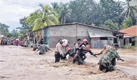  ?? FOTO: DPA ?? Soldaten und Polizisten helfen Anwohnern über eine überflutet­e Straße. Dutzende Menschen sind durch Schlammlaw­inen getötet worden, Tausende mussten sich in Sicherheit bringen, wie hier auf der indonesisc­hen Insel Lembata östlich von Bali.