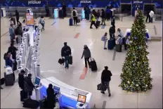  ?? CHARLES KRUPA — THE ASSOCIATED PRESS ?? Travelers pass a Christmas tree while heading toward the Terminal C gates at Logan Internatio­nal Airport on Monday in Boston.