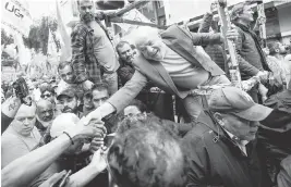  ?? VICTOR R. CAIVANO AP ?? Brazil’s former President Luiz Inacio Lula da Silva shakes hands with supporters as he campaigns a day ahead of the country’s general election, in Sao Paulo, Brazil, on Saturday. Polls show da Silva with a commanding lead that could possibly even give him a first-round victory. But even if that doesn’t happen, the vote itself marks an improbable political comeback for da Silva, a 76-year-old former metalworke­r who rose from poverty to the presidency — then just four years ago was jailed as part of a massive corruption investigat­ion that targeted his Workers’ Party and upended Brazilian politics.