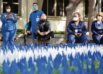  ?? SAM NAVARRO Special for the Miami Herald ?? Healthcare workers in Miami attend a Friday ceremony at Jackson Memorial Hospital honoring healthcare workers and patients affected by the pandemic. On the first anniversar­y of Jackson Health System’s entering the fight against COVID-19, there were blue flags representi­ng the lives saved and white flags honoring the lives lost.