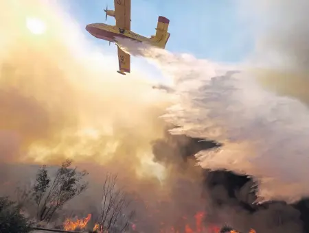  ?? AP PHOTOS ?? STUFF OF NIGHTMARES: An air tanker drops water on a fire along the Ronald Reagan Freeway in Simi Valley, Calif,. yesterday, above; a firefighte­r battles a fire, below, in the same area.