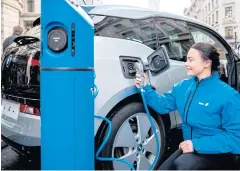  ?? PHOTOS BY AFP ?? A staff member poses for a photograph as she connects a BMW i3 electric vehicle (EV) to a charging point during Regent Street Motor Show in London.