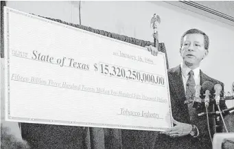  ?? San Antonio Express-News file ?? Texas Attorney General Dan Morales shows a symbolic check with the amount of the tobacco suit settlement in January 1998. The eventual settlement was $17.6 billion.