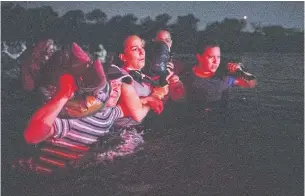  ?? REUTERS ?? Asylum-seeking migrants from Nicaragua lock arms as they wade across the Rio Grande River into the US from Mexico, in Roma, Texas on Wednesday.