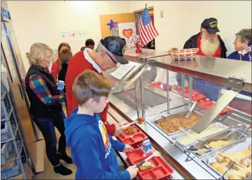  ??  ?? Liam Sanders (front blue sweatshirt) and his grandfathe­r U.S. Army veteran Wayne Kirsch (black ball cap) help themselves to lunch at East Central Elementary School on Monday morning. The schools provided free lunch, coffee and dessert for all veterans who came to eat with a family member.