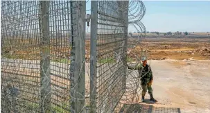  ?? —AFP photos ?? Israeli soldiers stand near the border with Syria in occupied Golan Heights as they prepare to evacuate a wounded Syrian for treatment, and (right), an Israeli soldier stands along the fence.