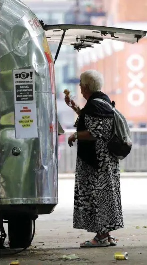  ??  ?? A woman buys an ice-cream at Gabriel’s Wharf beside the River Thames in London yesterday. The government has been easing stay-at-home orders imposed in late March with pubs, restaurant­s and museums reopening today.