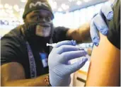  ?? TED S. WARREN AP ?? DeMarcus Hicks, who is working as a contractor with the Federal Emergency Management Agency, gives a patient a Pfizer booster shot in Federal Way, Wash.