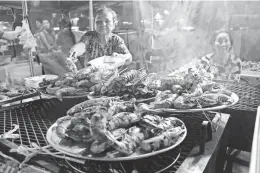  ??  ?? Women grill giant prawns at the Asian Garden Mall night market.