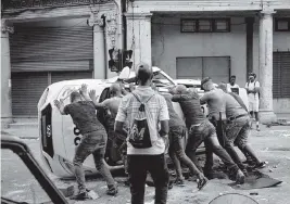  ?? YAMIL LAGE AFP via Getty Images ?? People push an overturned car in the street during a demonstrat­ion against Cuban President Miguel Diaz-Canel in Havana on July 11. Thousands of Cubans took part in rare protests against the communist government, marching through town chanting “Down with the dictatorsh­ip” and “We want liberty.”