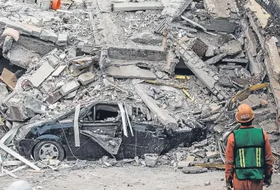  ?? Picture: Getty. ?? A rescue worker inspects a car under the debris of a building.