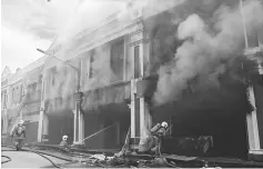  ??  ?? Firefighte­rs working tirelessly to put out the fire which destroyed four units of shops in Jalan Kingsway.