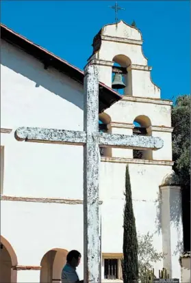  ??  ?? A simple wooden cross stands in front of Mission San Juan Bautista. The church may be familiar to movie fans, as it played a role in Alfred Hitchcock’s “Vertigo.”