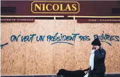 ?? KAMIL ZIHNIOGLU/ASSOCIATED PRESS ?? A woman walks by graffiti on a wine shop reading “We want a president for the poor” near the Arc de Triomphe in Paris on Sunday.
