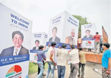  ??  ?? Workers carry a hoarding featuring Modi and Abe to load it onto a truck ahead of Abe’s visit, in Ahmedabad, India. — Reuters photo