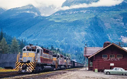  ?? ?? A westbound freight train with three SD40s passes rustic the Glacier station on Aug. 13, 1969. The train has just exited Connaught Tunnel bored through Mount MacDonald in the Selkirks; the concrete portal is barely visible above the second hopper car.