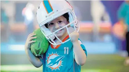  ?? MIKE STOCKER/SOUTH FLORIDA SUN SENTINEL ?? Gabriel Dies, 5, tries to hold on to his helmet Saturday as he runs with the ball.