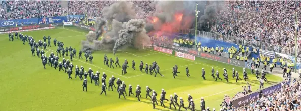  ?? FOTO: DPA ?? Polizei marschiert auf, um einen Platzsturm zu verhindern, Randaliere­r im HSV-Block haben Pyrotechni­k gezündet und Böller in den Gladbacher Strafraum geworfen.