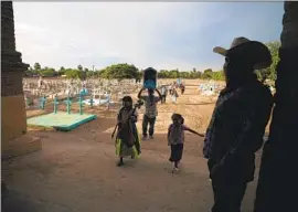  ?? Fernando Llano Associated Press ?? A YAQUI Indigenous family pass the cemetery in Potam, Mexico, where water rights defender Tomás Rojo is buried. He was among the activists killed last year.