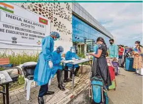  ?? AFP PIC ?? High Commission officials and volunteers in protective gear checking Indian citizens for visa procedures before they board a ship to be evacuated to India due to the Covid-19 pandemic, at a bus station in Male, Maldives, last year.