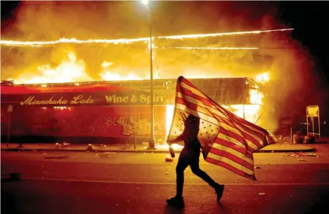  ?? Foto: dpa/Julio Cortez ?? Demonstran­t in Minneapoli­s mit einer als Protestsym­bol umgedrehte­n US-Flagge vor einem brennenden Getränkema­rkt